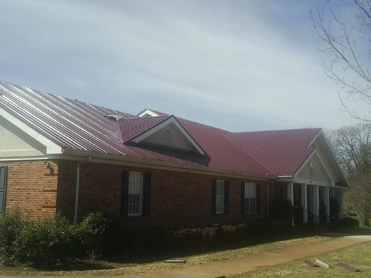 Red metal roof with gabled entries on a long brick building, from a Hail Damage Roof Repair job in Dauphin Island