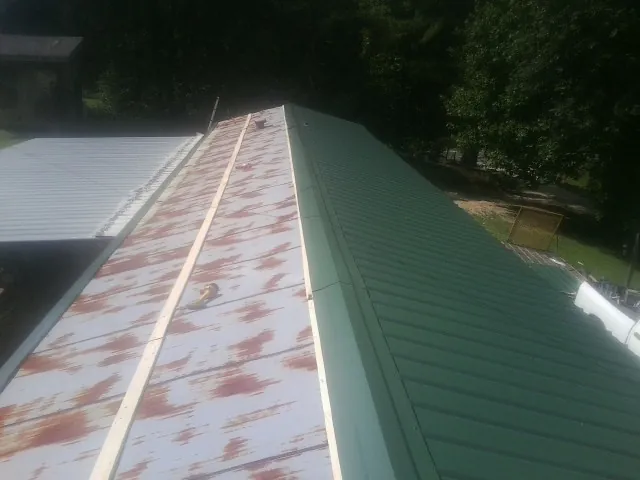Old rusted panels beside newly installed green metal roofing — Wind Damage Roof Repair by Roofing Brothers in Dauphin Island