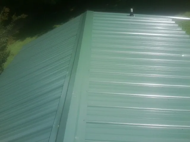 New green metal panels meeting at the ridge of a roof — Flat Roof Repair work by our crew in Dauphin Island