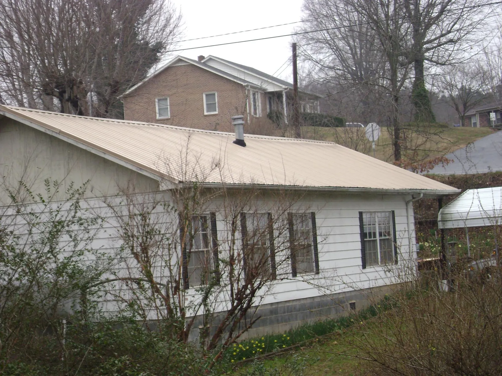 Tan metal roof on a white sided house set into a hillside — Commercial Roofing by Roofing Brothers in Dauphin Island